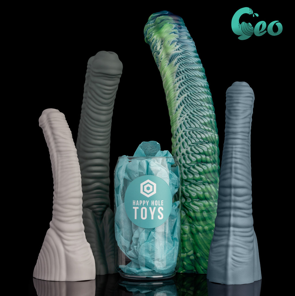 Four Geo dildos in four colors. There is a clear plastic "soda can" filled with teal tissue paper in the middle for scale. From left: Small in Tapioca, Large in Clay Creek, XLarge in Seacock Spirit (Premium Pour), and Medium in Fjord.